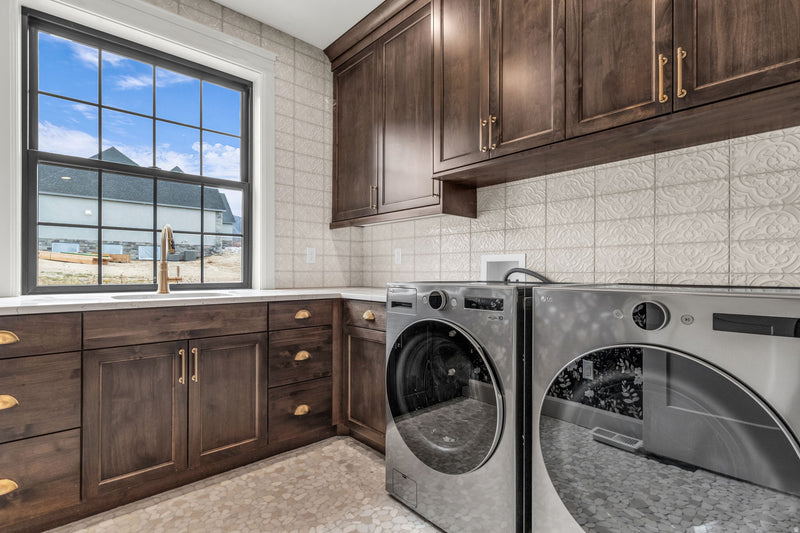 Luxury laundry room with dark wood shaker cabinets, gold hardware, quartz countertop, farmhouse sink, and textured tile backsplash