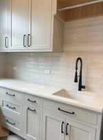 Modern laundry room with white cabinets, black fixtures, and a tiled backsplash.