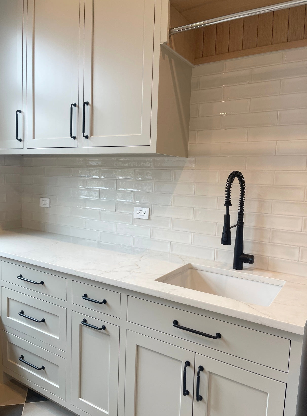 Modern laundry room with white cabinets, black fixtures, and a tiled backsplash.