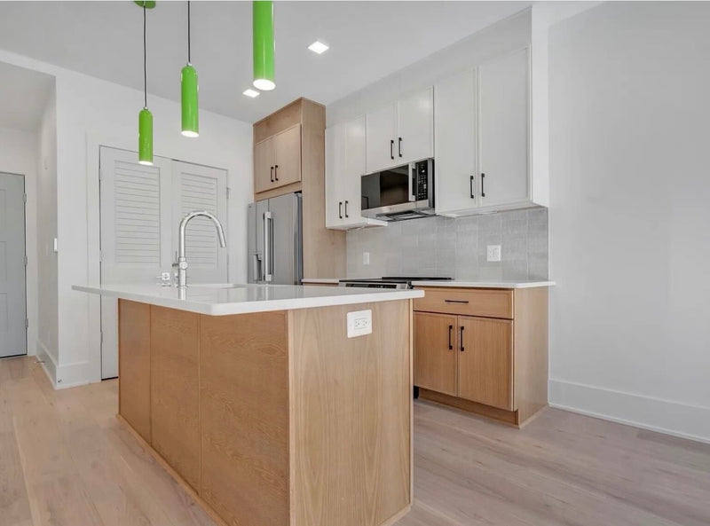 Modern two-tone kitchen with white upper cabinets, natural wood lower cabinets and island, white quartz countertop, and statement green pendant lights