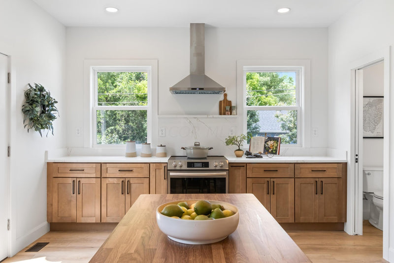 Shaker base cabinets with white quartz countertops, stainless range hood, and butcher block island in bright natural light kitchen