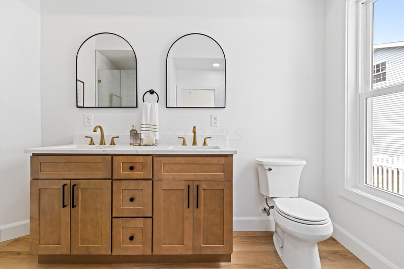 Double vanity with white quartz countertop, gold faucets, matte black hardware, arched black mirrors, and light hardwood floors