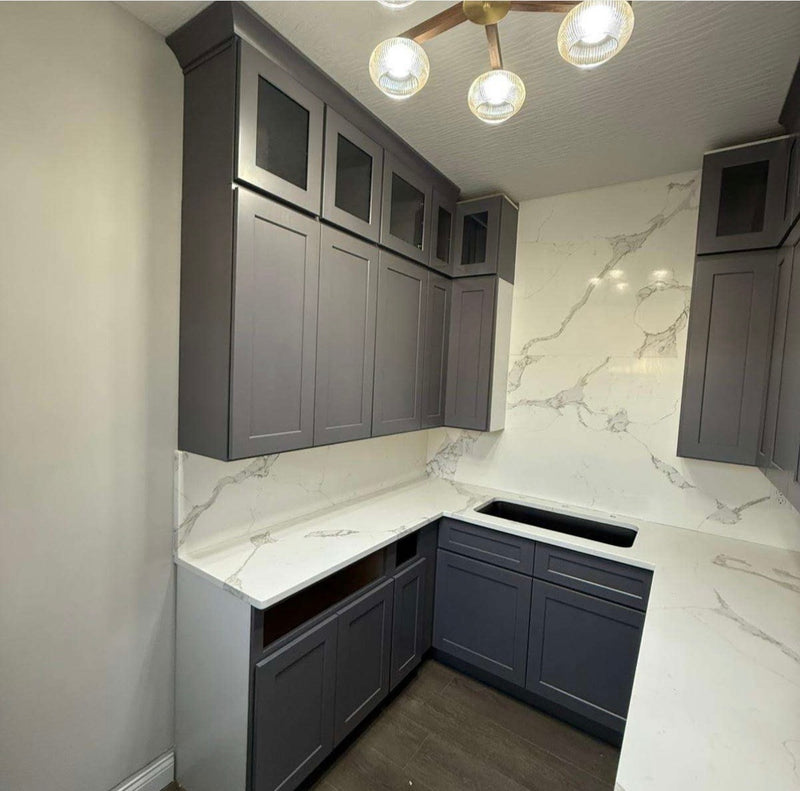 Wet bar with gray shaker cabinets, stacked glass-front upper cabinets, full-height marble quartz backsplash, and undermount sink