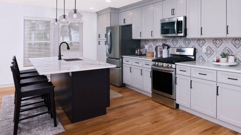 Two-tone kitchen with light gray shaker cabinets, black island, white marble quartz countertop, geometric diamond tile backsplash, matte black hardware, and hardwood floors