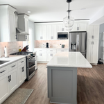 A kitchen featuring Rose Hill white shaker cabinets, a gray island, LVT flooring, marble backsplash, and glass pendant lighting