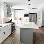 A kitchen featuring Rose Hill white shaker cabinets, a gray island, LVT flooring, marble backsplash, and glass pendant lighting
