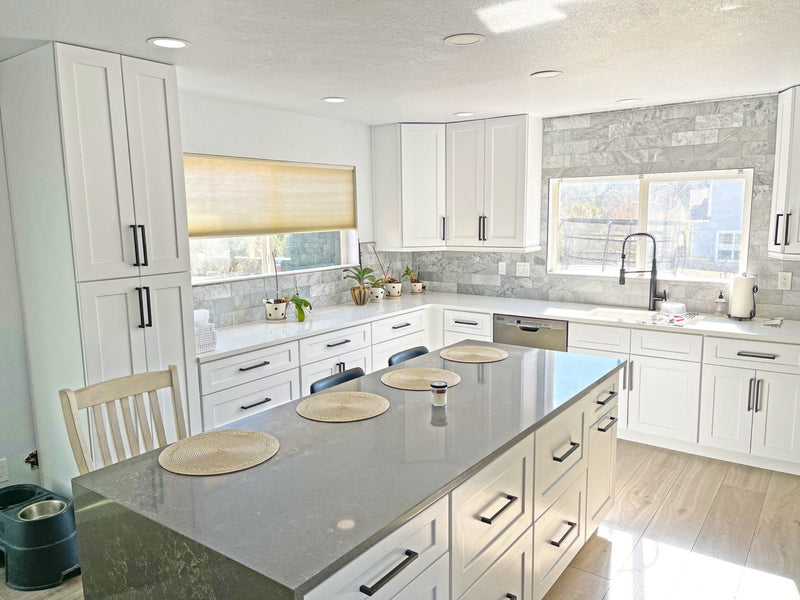 White shaker kitchen cabinets with matte black hardware, gray quartz island, marble tile backsplash, and tall pantry cabinet