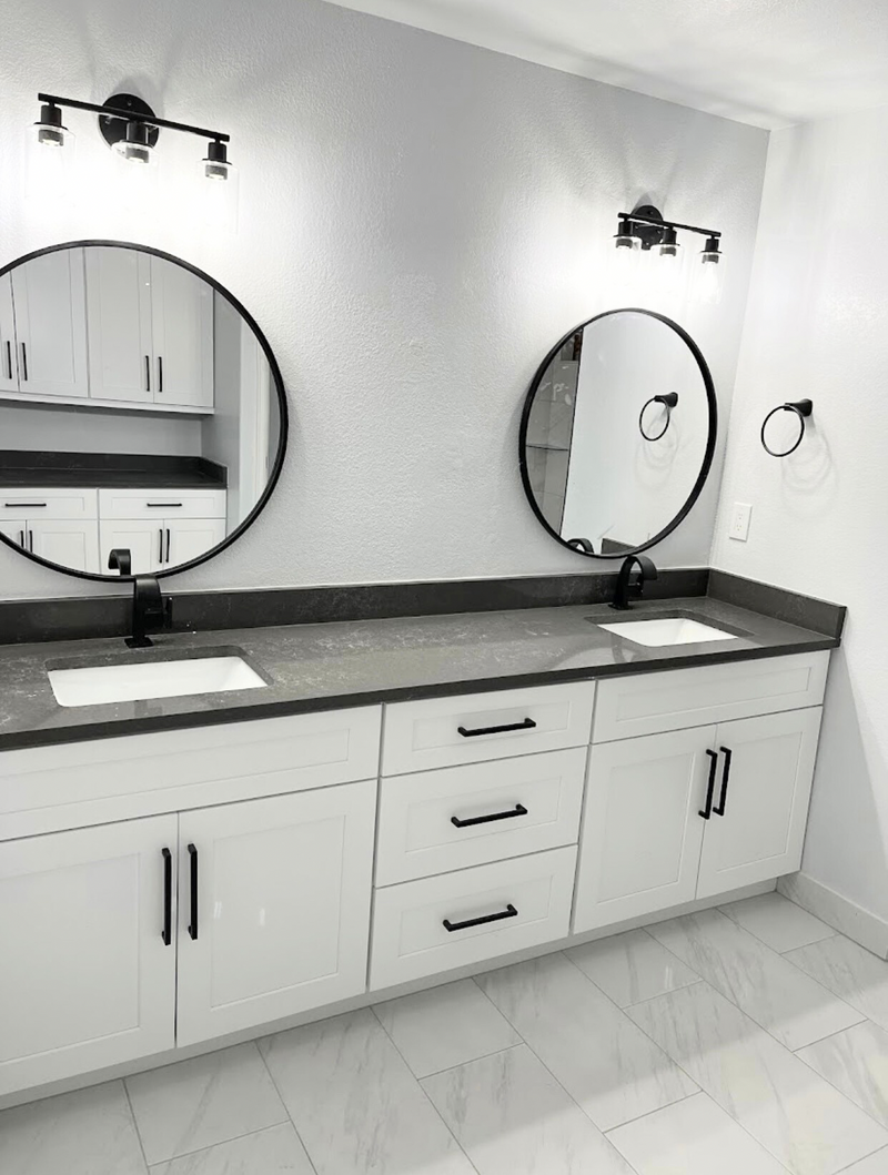 White shaker double vanity with dark quartz countertop, matte black hardware, round mirrors, and marble porcelain tile floor