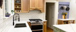 Modern kitchen with light wooden cabinets, sage green island, stainless steel appliances, and a white subway tile backsplash.