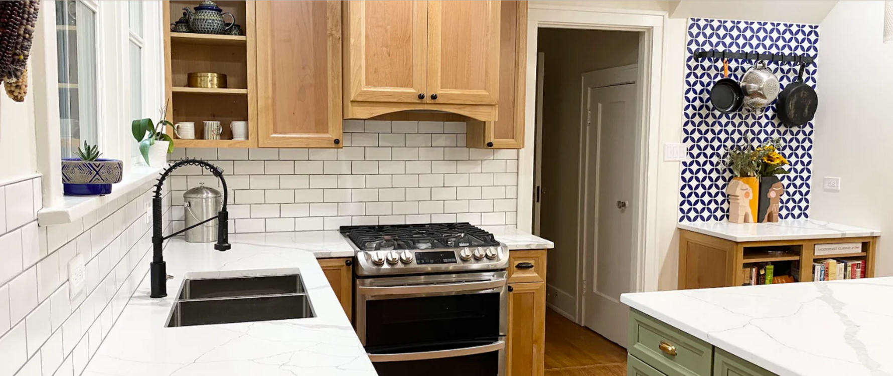 Modern kitchen with light wooden cabinets, sage green island, stainless steel appliances, and a white subway tile backsplash.